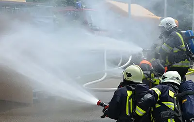 Feuerwehrmänner, die dicht nebeneinander stehen und mit dem Löschschlauch Wasser verspritzen.